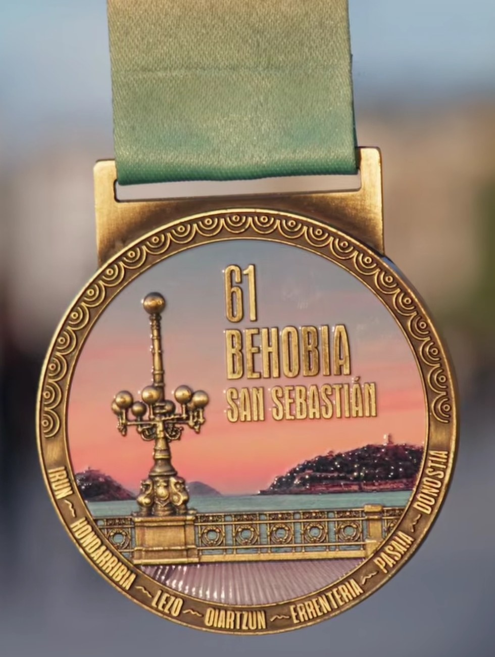 Medalla de la 61.ª Behobia – San Sebastián con la farola de La Concha al atardecer