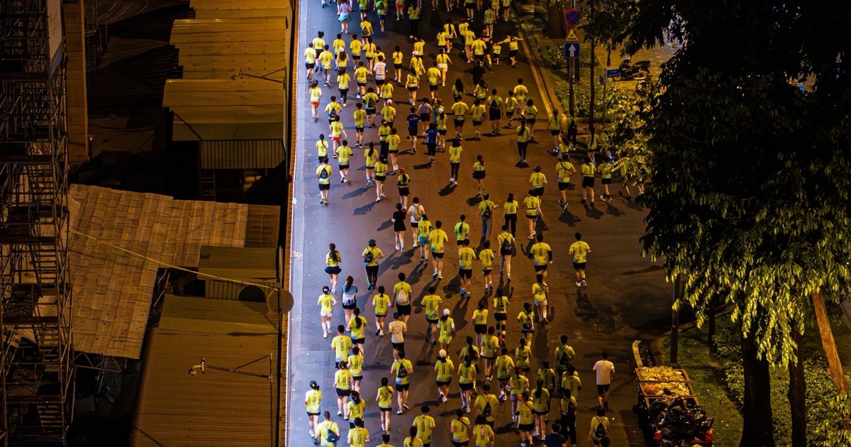 Una multitud de corredores con camisetas amarillas por una calle iluminada de noche