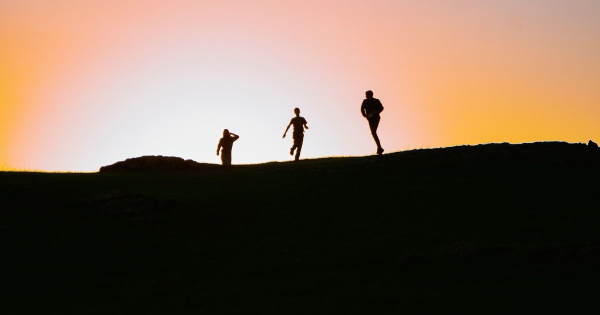 Tres corredores en silueta sobre una colina al atardecer