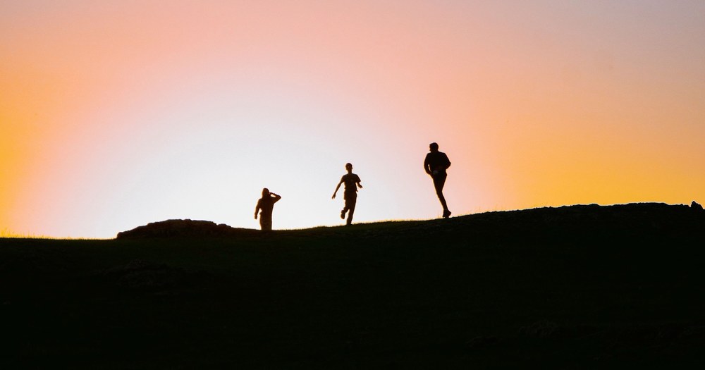 Tres corredores en silueta al atardecer sobre una colina