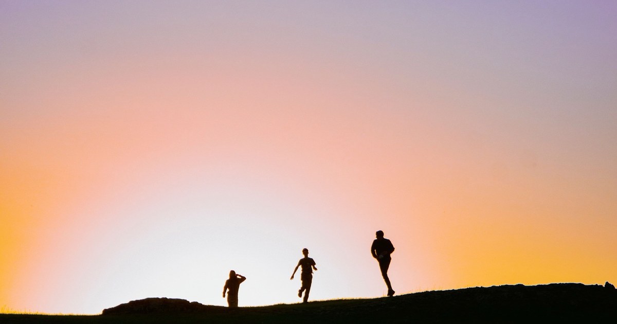Tres corredores en silueta sobre una colina al atardecer
