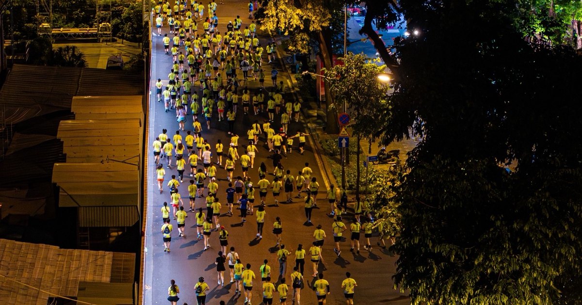Un río de corredores con camiseta amarilla por una calle iluminada de noche