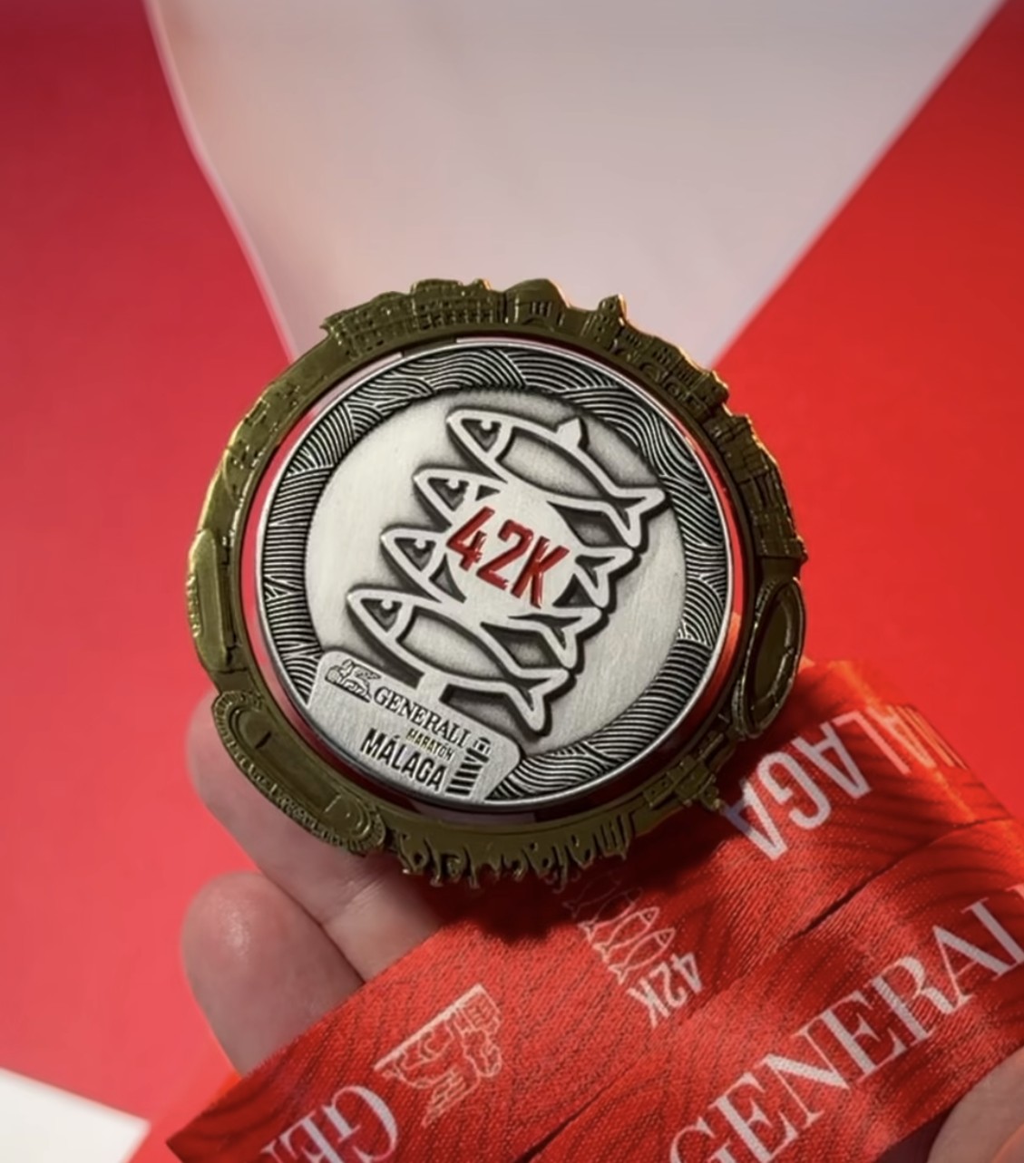 Medalla de la 42K del Generali Maratón Málaga 2026 sostenida en la mano sobre fondo rojo