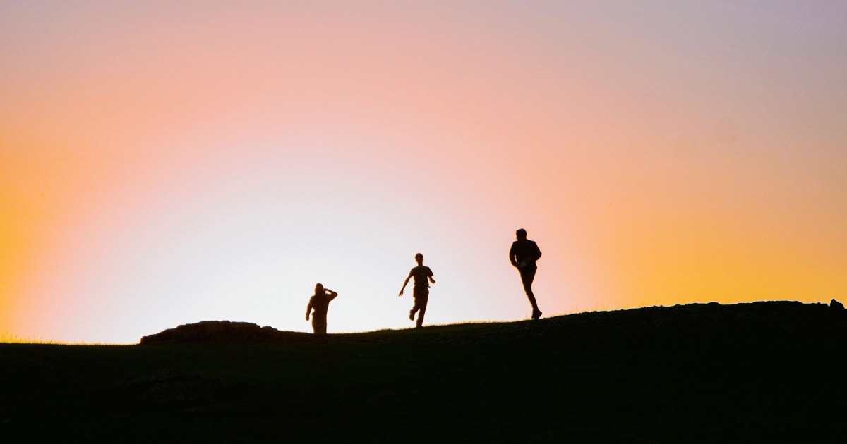 Siluetas de tres corredores sobre una loma al atardecer