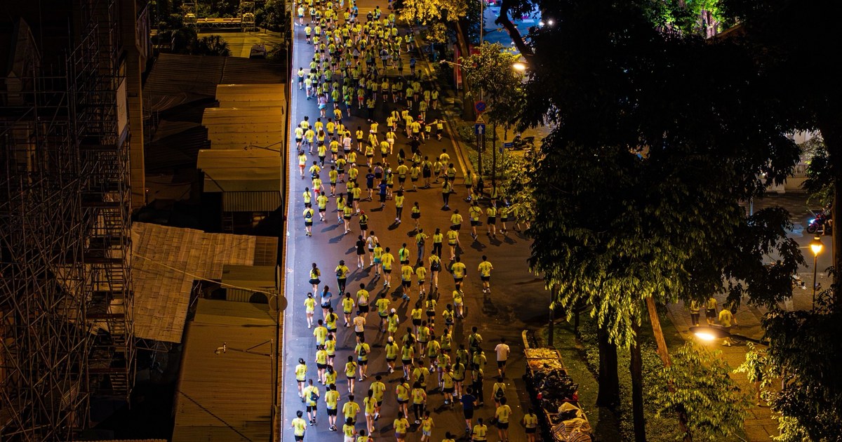 Marea de corredores con camisetas amarillas por una calle de noche