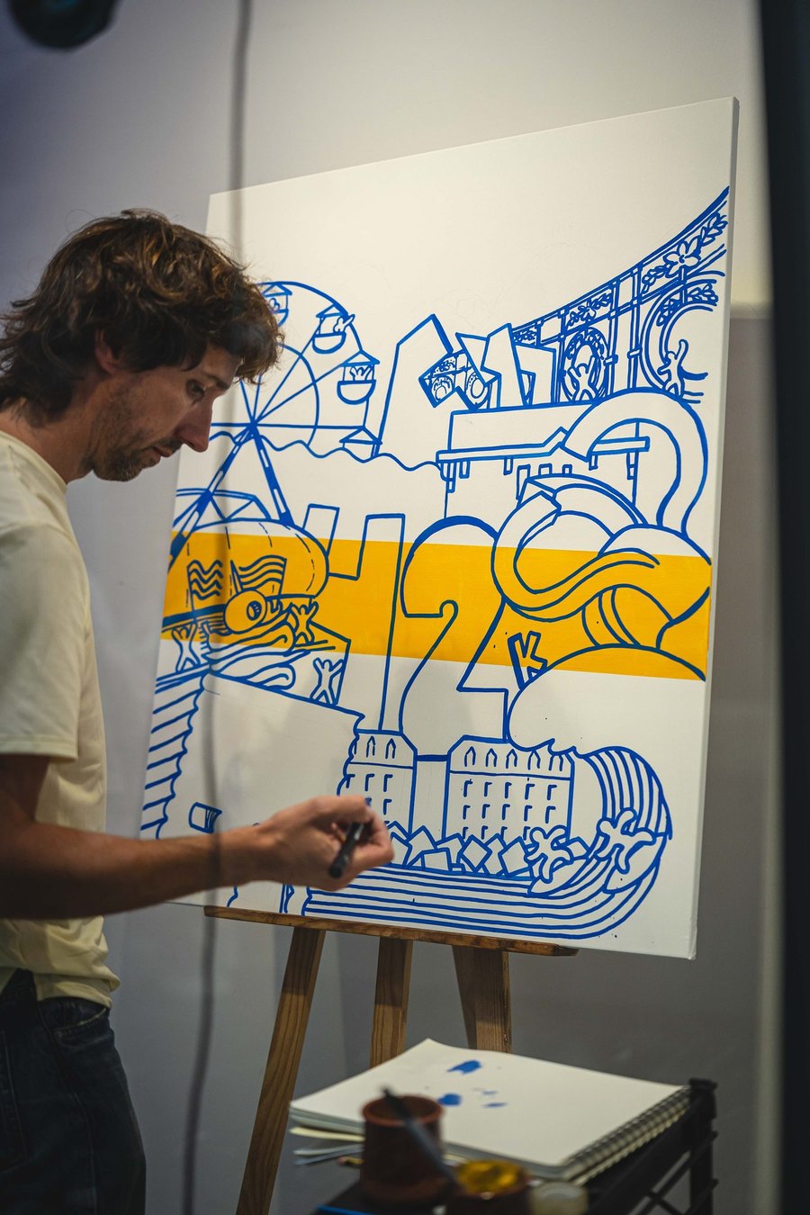 Mikel Soro dibujando en directo el diseño de la camiseta sobre un lienzo con una noria, edificios y olas